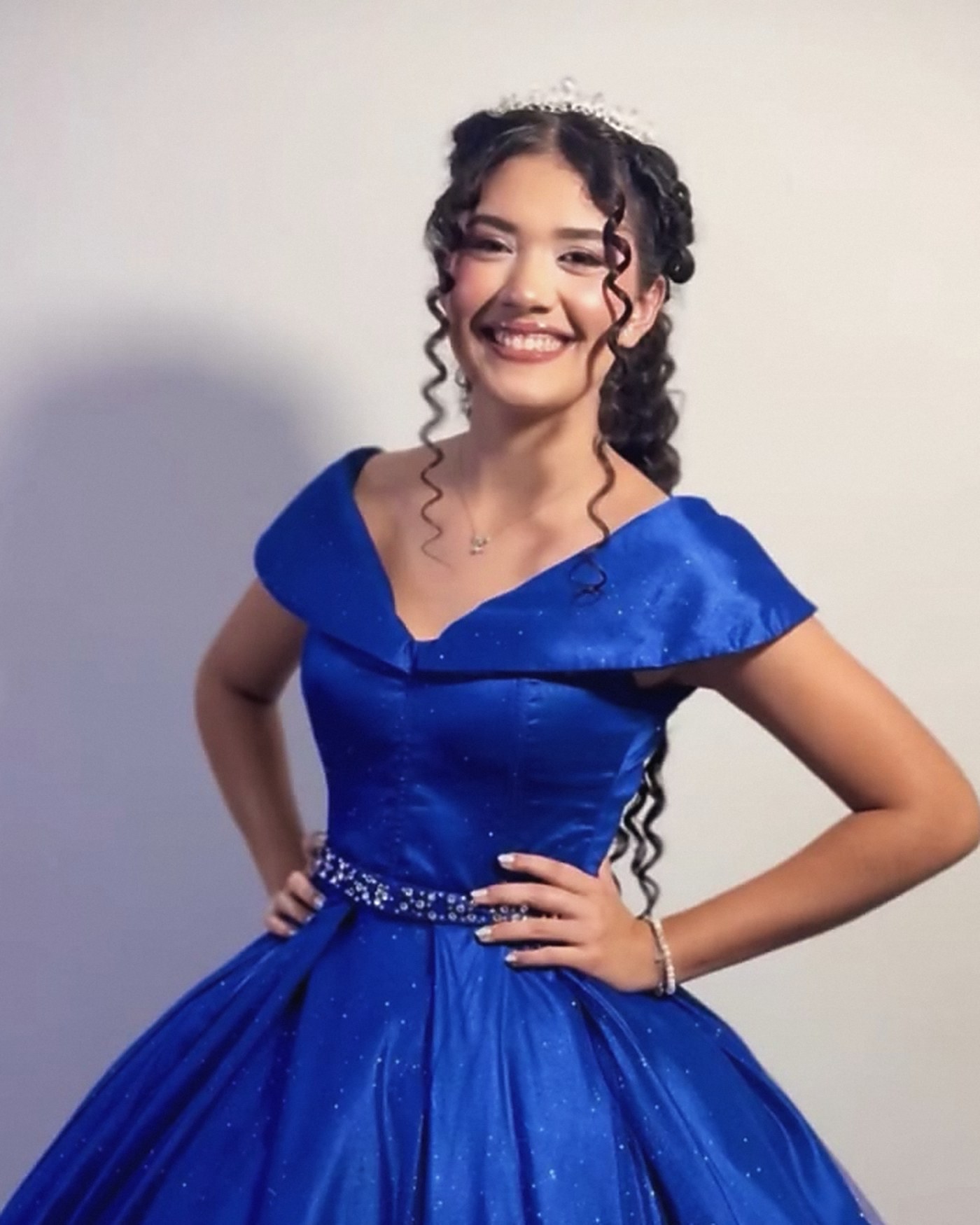 Debutante sorrindo com vestido azul, tiara e cachos definidos