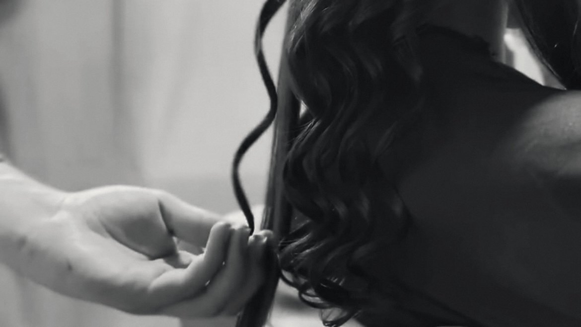 Mão ajustando os cachos de um penteado para evento, em preto e branco