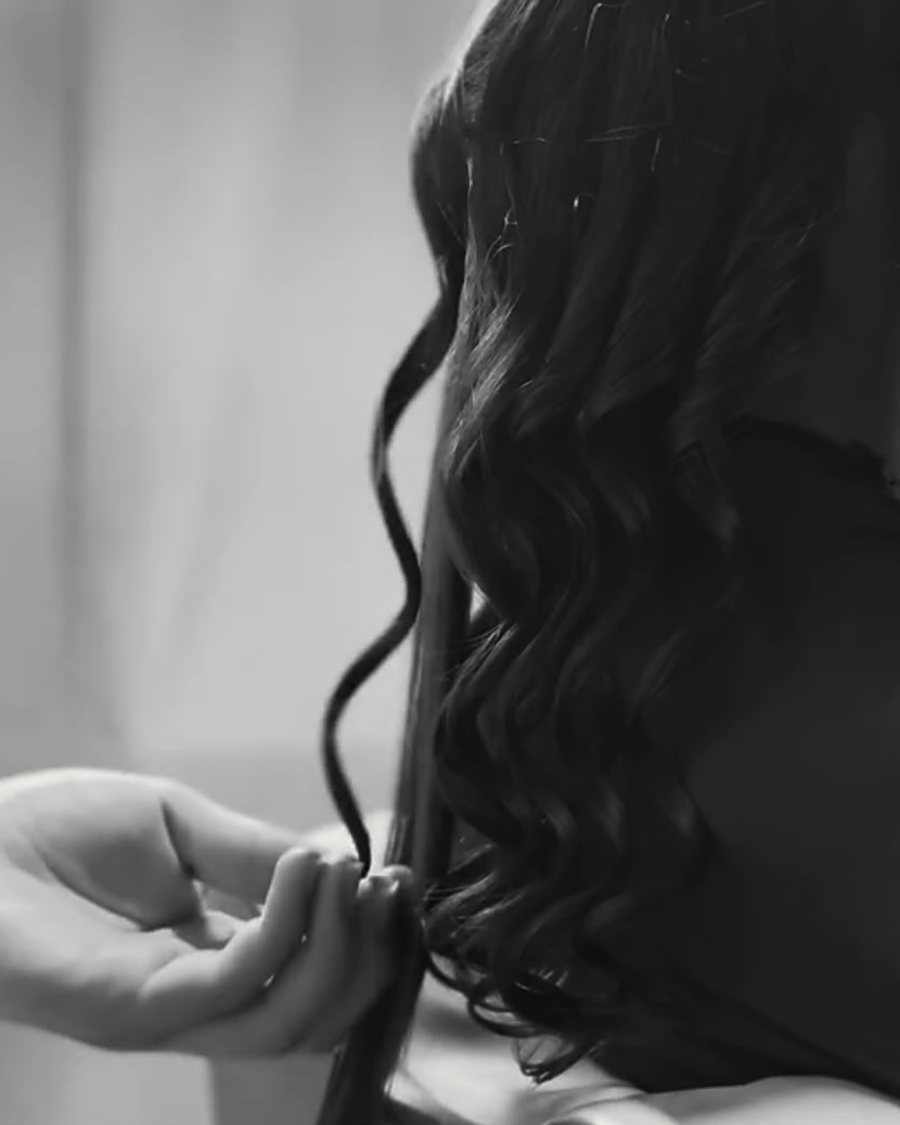 Mão finalizando os cachos de um penteado, em preto e branco